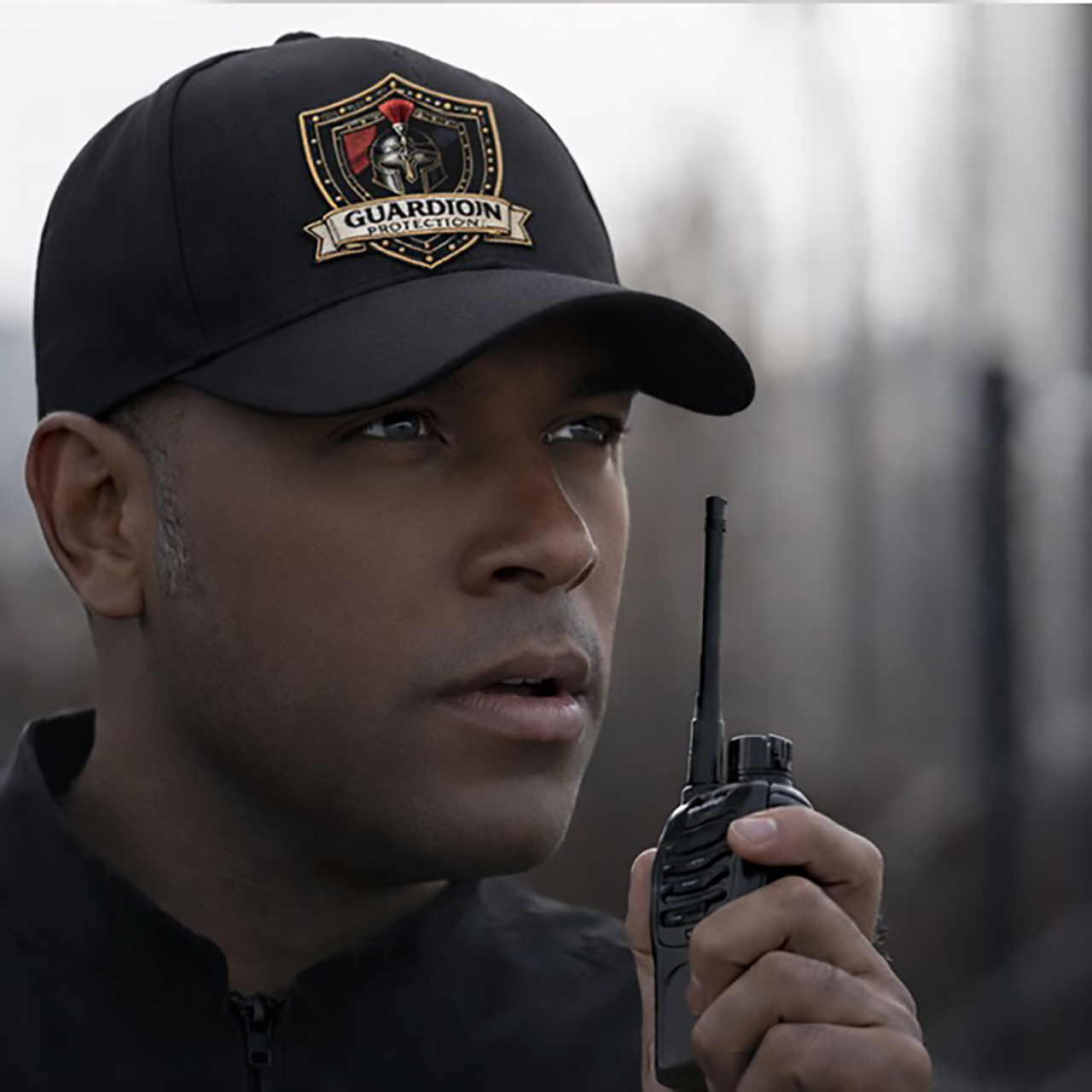 Guardion Protection private security officer in a black tactical cap and uniform providing professional surveillance and rapid communication.